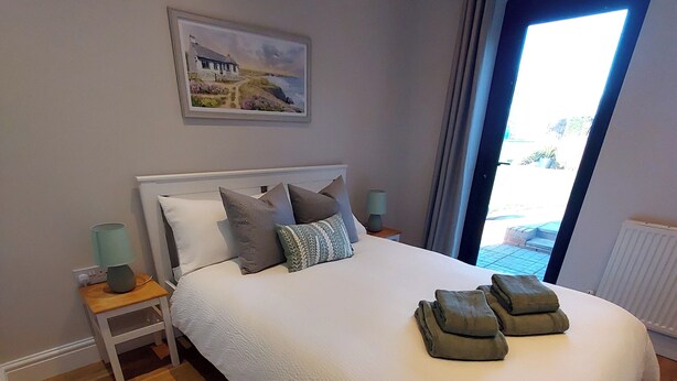A bedroom with a large bed, a nightstand, a lamp, a rug, and a window with curtains. - The Annex @ Holly Glenn a cosy couple's retreat (Clint Green)