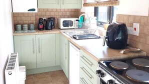 A compact kitchen with light green cabinets, a white refrigerator, a stove, and a coffee maker. - The Annex @ Holly Glenn a cosy couple's retreat (Clint Green)