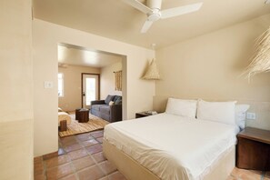 Un dormitorio con una cama grande, un ventilador de techo, una mesita de noche y una lámpara de mimbre.