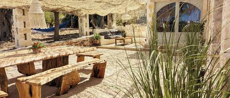 An outdoor seating area with wooden benches and a table, surrounded by a woven canopy.