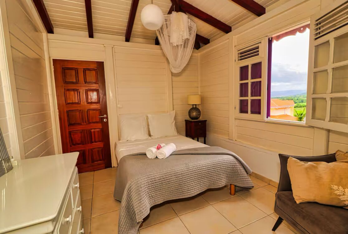 A bedroom with a bed, a bedside table, a lamp, a window with a view, and a door.