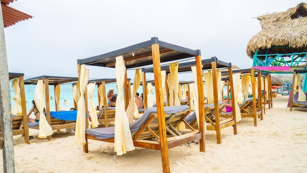 A beach with wooden beach chairs and thatched-roof structures.