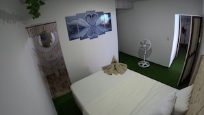A room with a bed, a wall-mounted fan, and a green carpet.