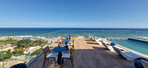 Um terraço com mesas e cadeiras, com vista para uma piscina e para o oceano.