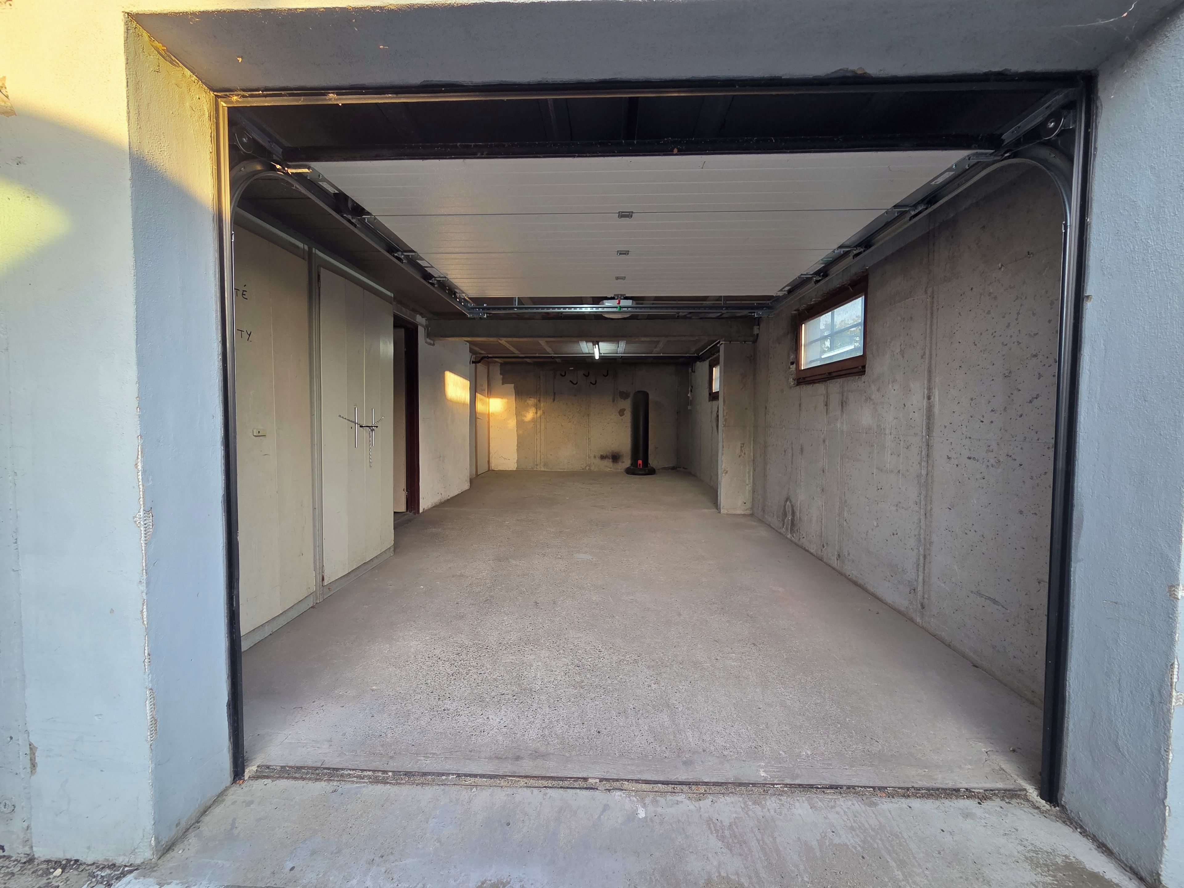 A concrete corridor with doors on both sides, leading to a room with a window.