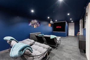A modern home theater room with a large flat-screen TV, reclining chairs, and a ceiling-mounted projector.