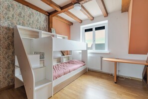 Ein Stockbett mit Stauraumregalen, einem kleinen Schreibtisch und einem Fenster mit Jalousien.