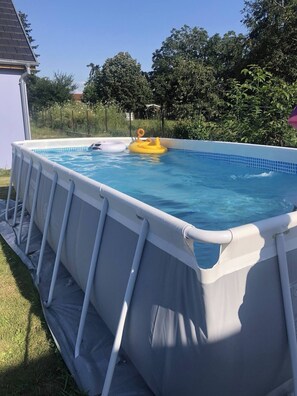 An above-ground swimming pool with a white inflatable cover, surrounded by a grassy yard and trees. - House for 10 | Garden, Pool & Cinema | 20 min Europa-Park (Witternheim)
