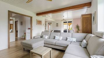 Un salon spacieux avec un grand canapé beige, une table basse en bois et un ventilateur de plafond.