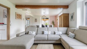 Una sala de estar moderna con un sofá modular, vigas de madera en el techo y vista al área de comedor.