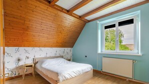 Ein Schlafzimmer mit Holzboden, einem Bett, einem Nachttisch, einem Fenster mit Blick und einer Heizung.