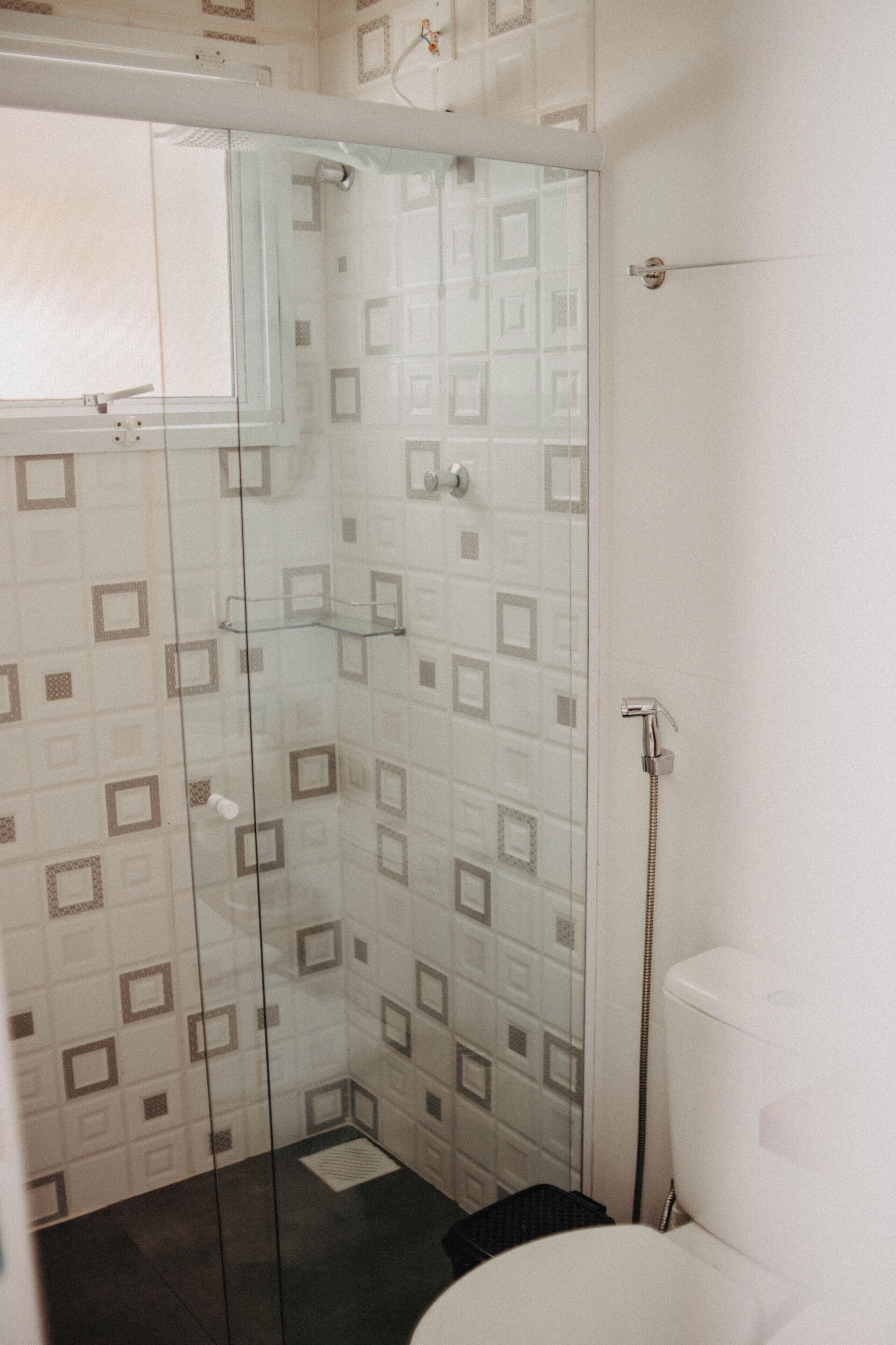 Een douche met glazen deur, betegelde wanden en een toilet.