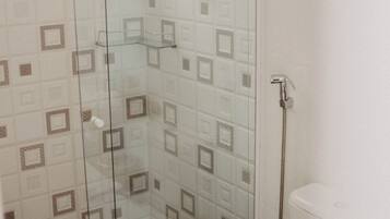 Een douche met glazen deur, betegelde wanden en een toilet.