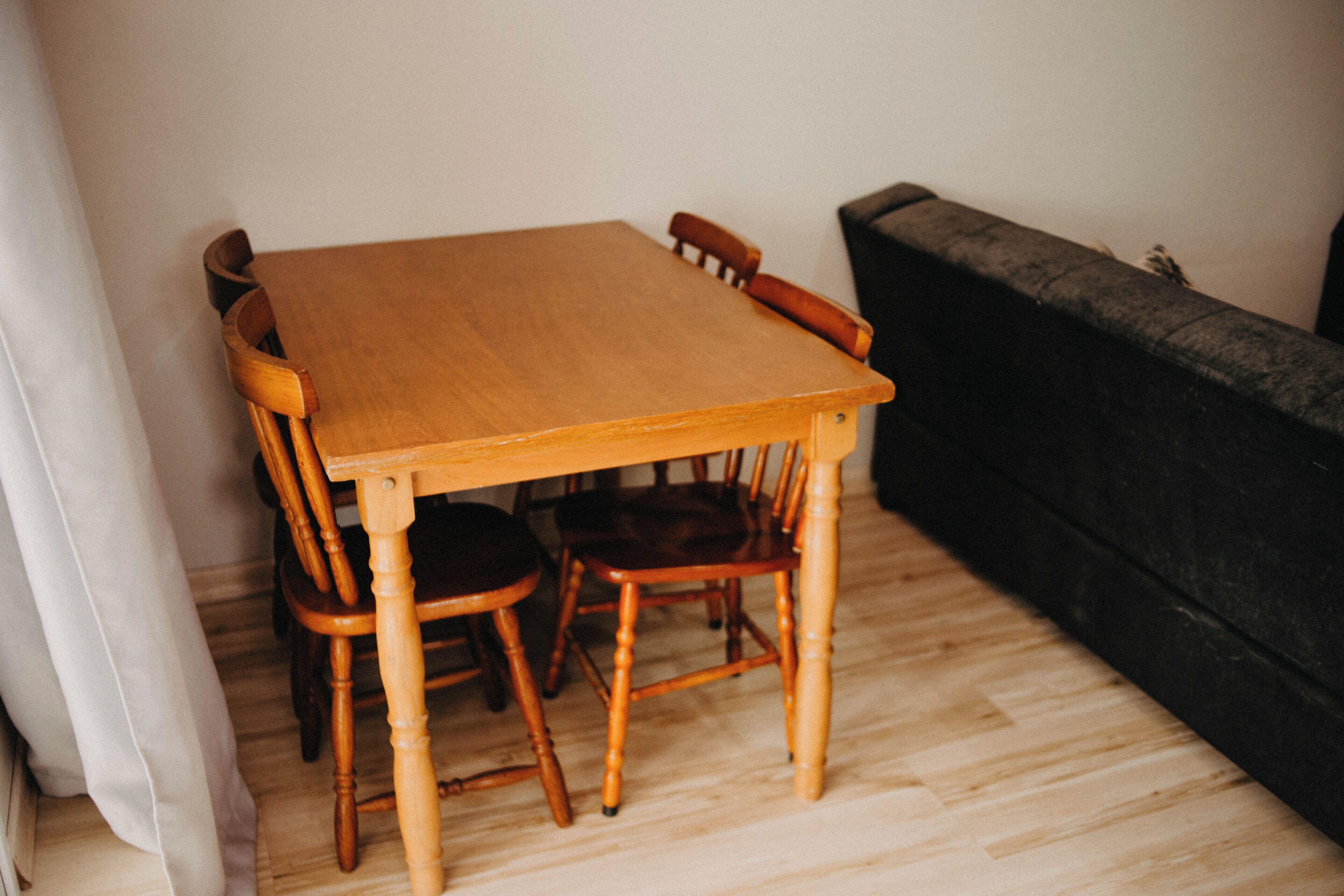 A wooden dining table with four chairs, a black sofa, and a white curtain.