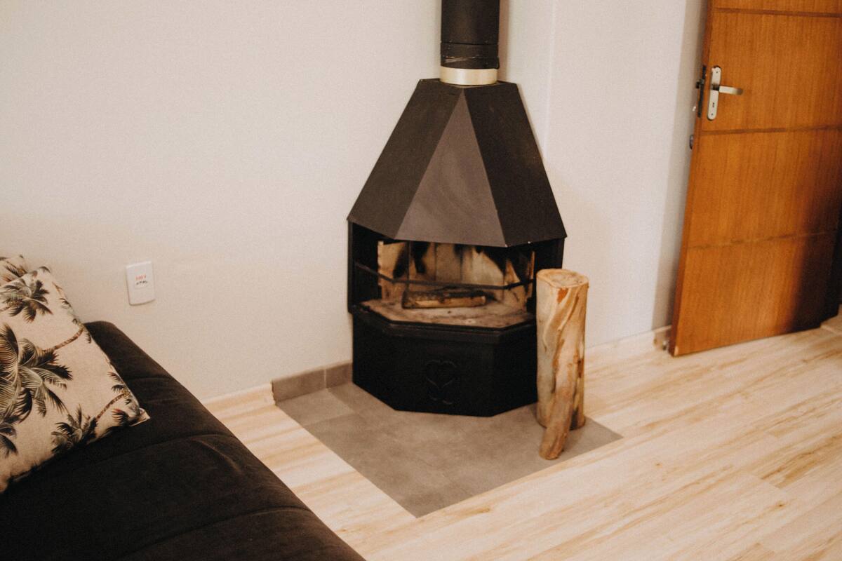 A room with a wood-burning stove, a wooden door, and a brown sofa with a patterned pillow.