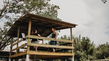 Une structure en bois dotée d’un toit, peut-être un belvédère ou un pavillon, entourée d’arbres.