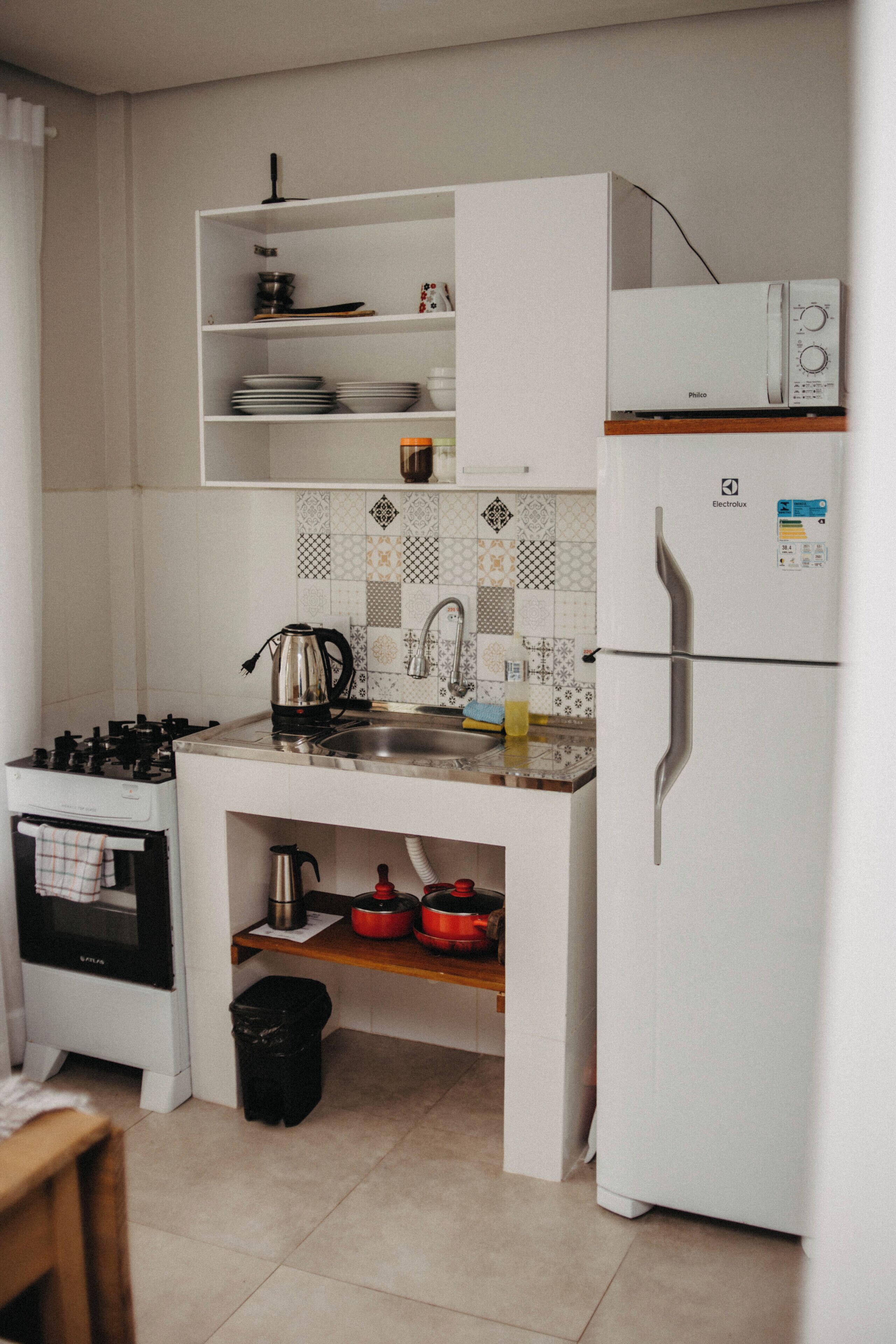 A compact kitchen with white cabinetry, a stove, a sink, and a refrigerator.