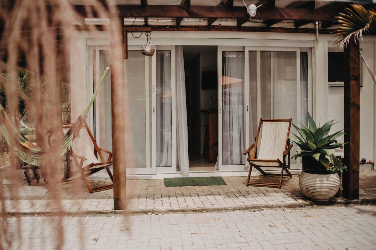 A covered patio area with a wooden chair, a potted plant, and a hammock.
