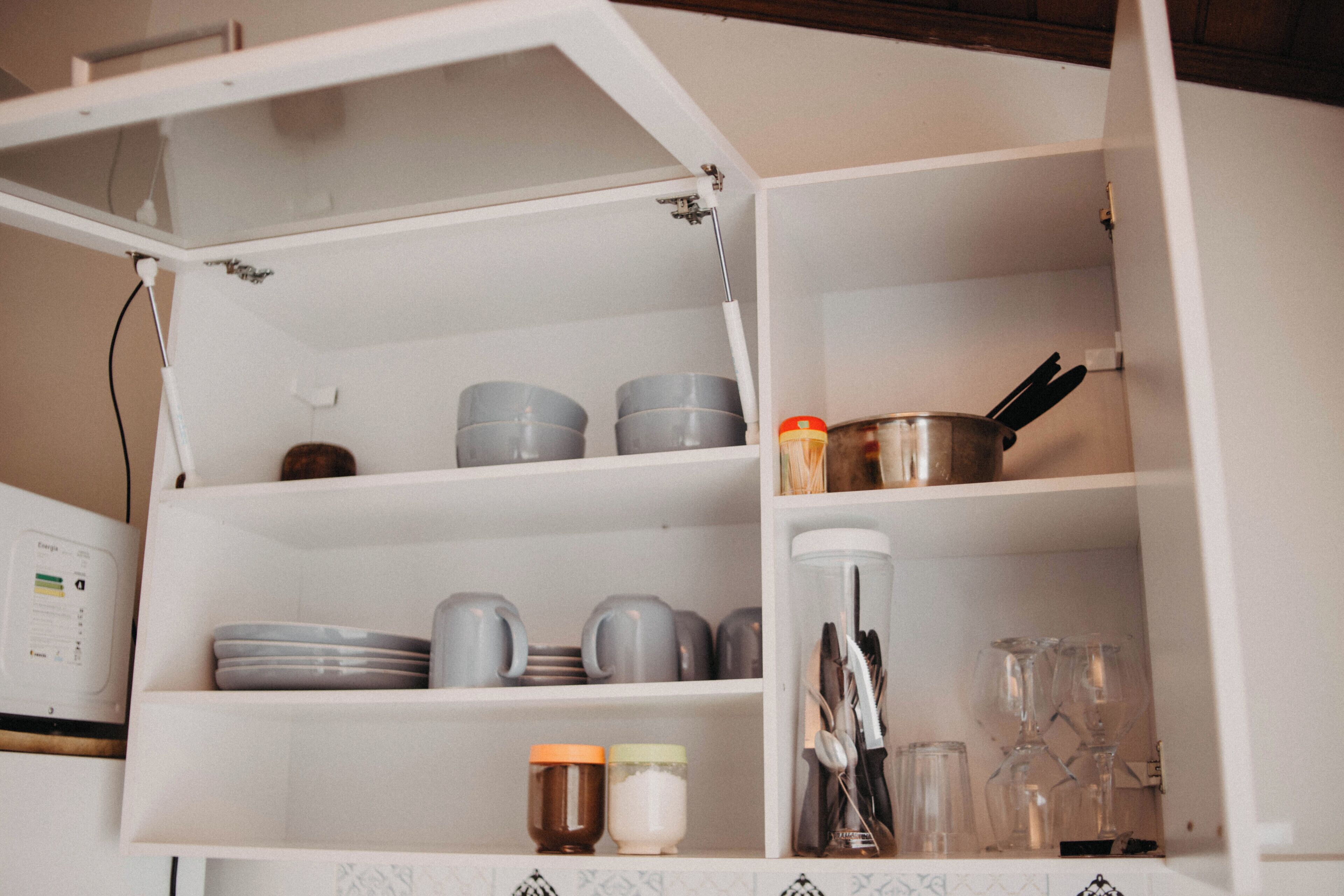 Une cuisine avec des meubles blancs, un four à micro-ondes et divers ustensiles de cuisine, notamment des assiettes, des tasses et des couverts.