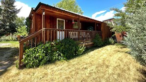 A wooden cabin with a porch, surrounded by greenery and trees.