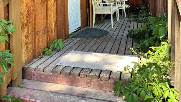 A wooden porch with a bench and chairs, a door, and a small garden area.