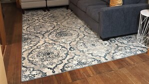 A living room with a grey sofa, two armchairs, a patterned rug, and a wooden floor.