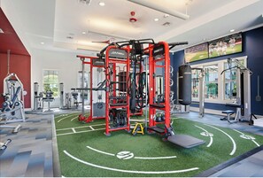 A gym with various exercise equipment, including a Smith machine and weight benches.