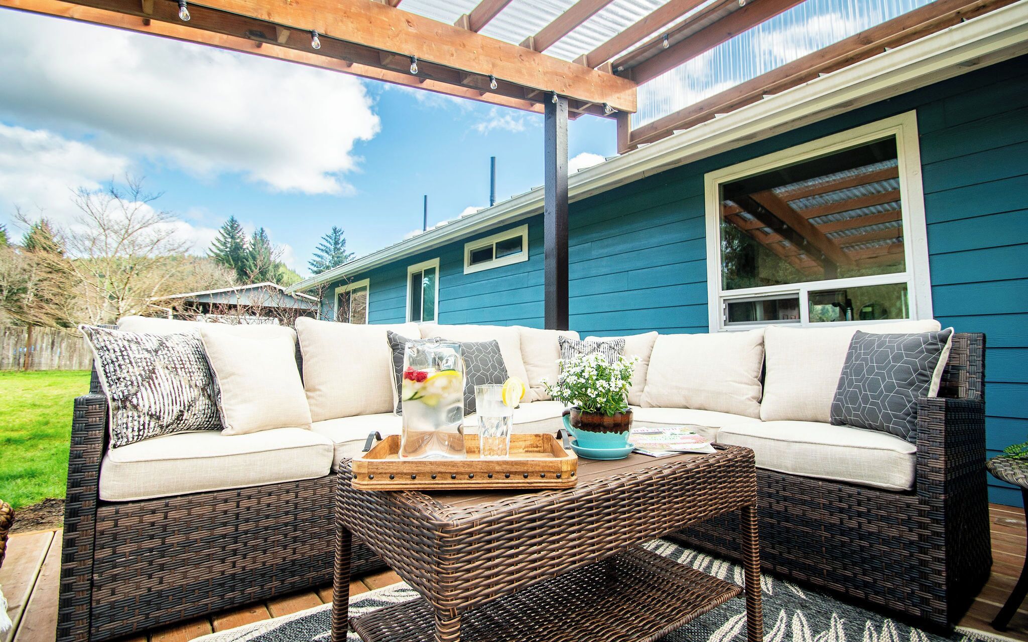 Une terrasse couverte avec un canapé en osier, une table basse et une plante en pot.