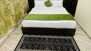 Une chambre à coucher avec un lit, une tête de lit à motifs, un plaid vert, un tapis noir et blanc et un luminaire fixé au mur.