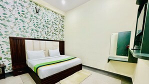 Une chambre à coucher avec un lit, une table de chevet, un miroir et un mur recouvert d’un papier peint à motifs floraux.