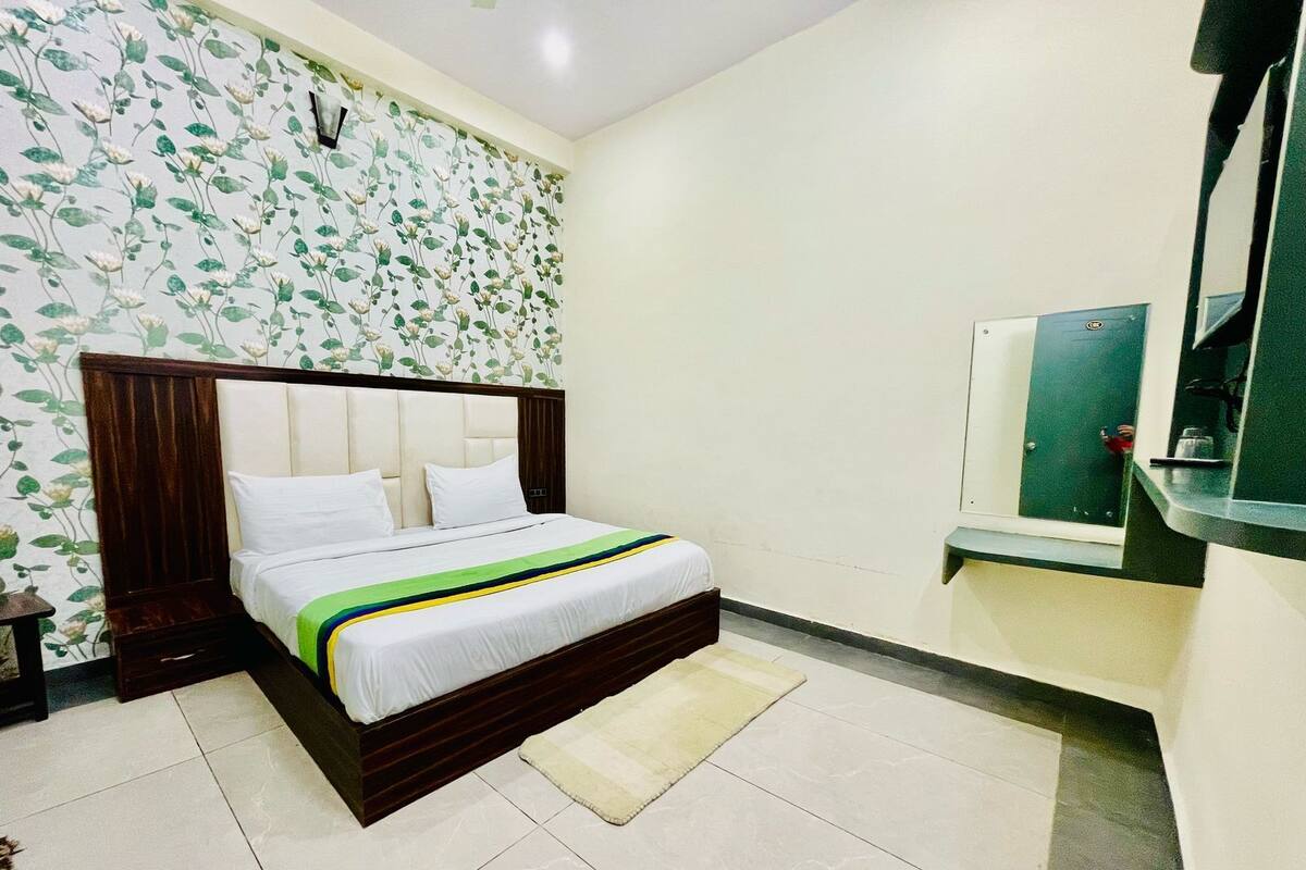 A bedroom with a bed, a nightstand, a mirror, and a wall with floral wallpaper.