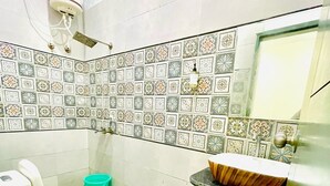 Une salle de bain comprenant des toilettes, un lavabo avec un récipient en bois, un seau vert et un mur recouvert de carreaux décoratifs.