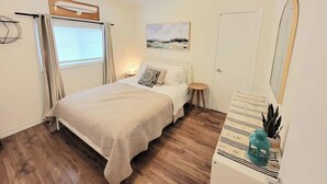 A bedroom with a bed, bedside table, lamp, and a painting on the wall.