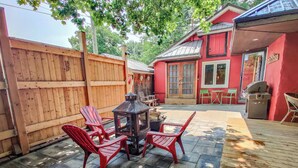 A backyard with a wooden deck, a red barbecue grill, and a wood-burning stove.