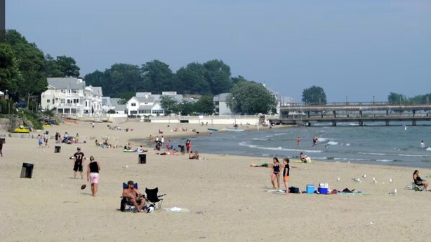 A beach with people, a pier, and houses in the background.