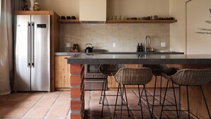 Een moderne keuken met een roestvrijstalen koelkast, een betegelde spatwand en een bar voorzien van rieten krukken.