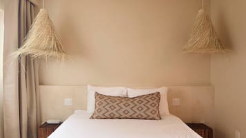Un dormitorio con cama, dos mesitas de noche, lámpara colgante y ventana con cortinas.