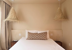 Un dormitorio con cama, dos mesitas de noche, lámpara colgante y ventana con cortinas.