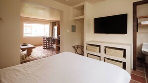 Een slaapkamer met een groot bed, een aan de muur bevestigde televisie en een klein tafeltje met stoelen.