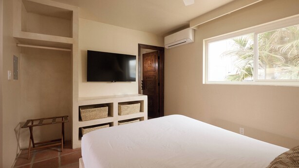Een slaapkamer met een bed, een aan de muur bevestigde televisie, een raam met uitzicht op palmbomen en een plafondventilator.