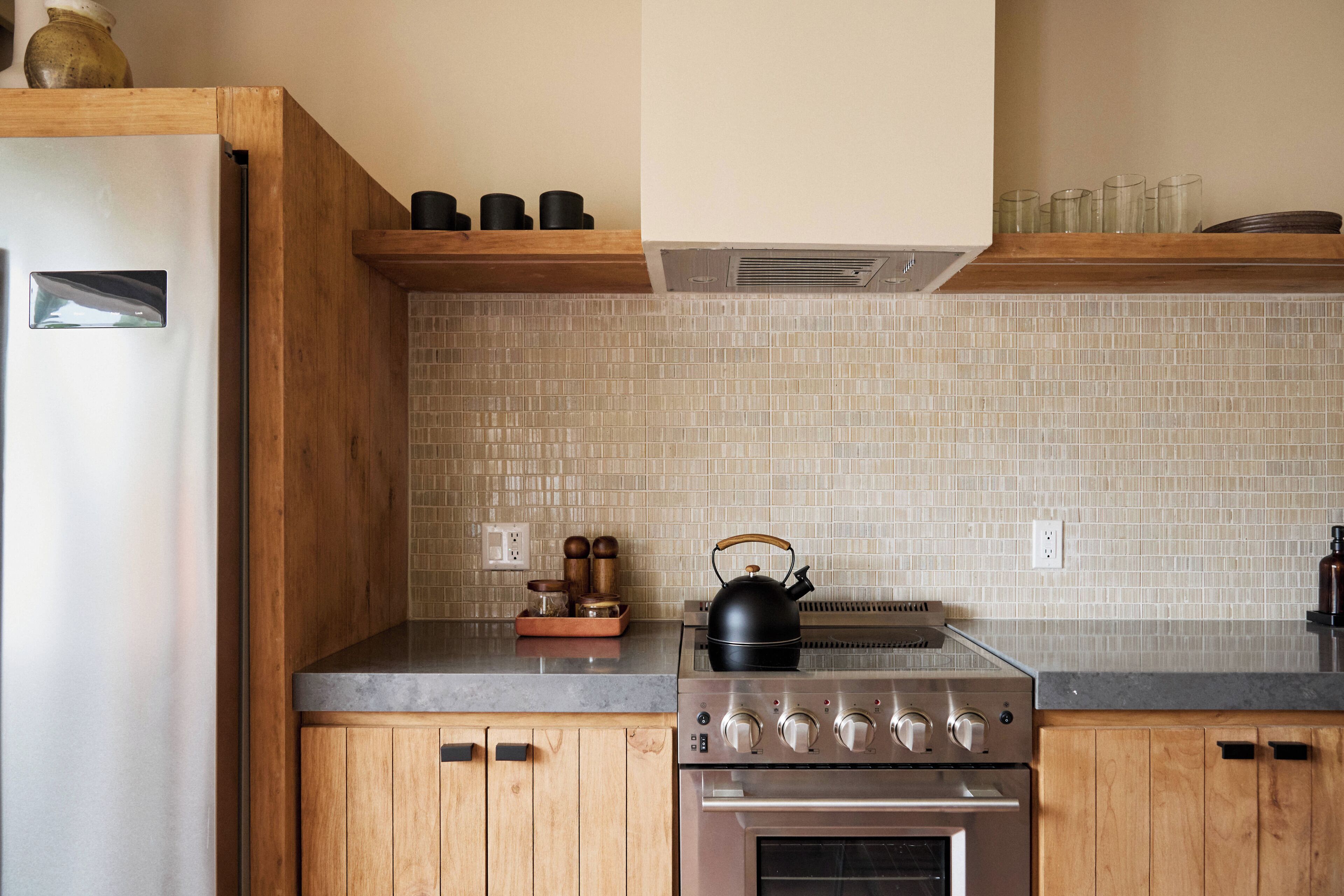 Una cocina con armarios de madera, un refrigerador de acero inoxidable, un hervidor y una estufa.
