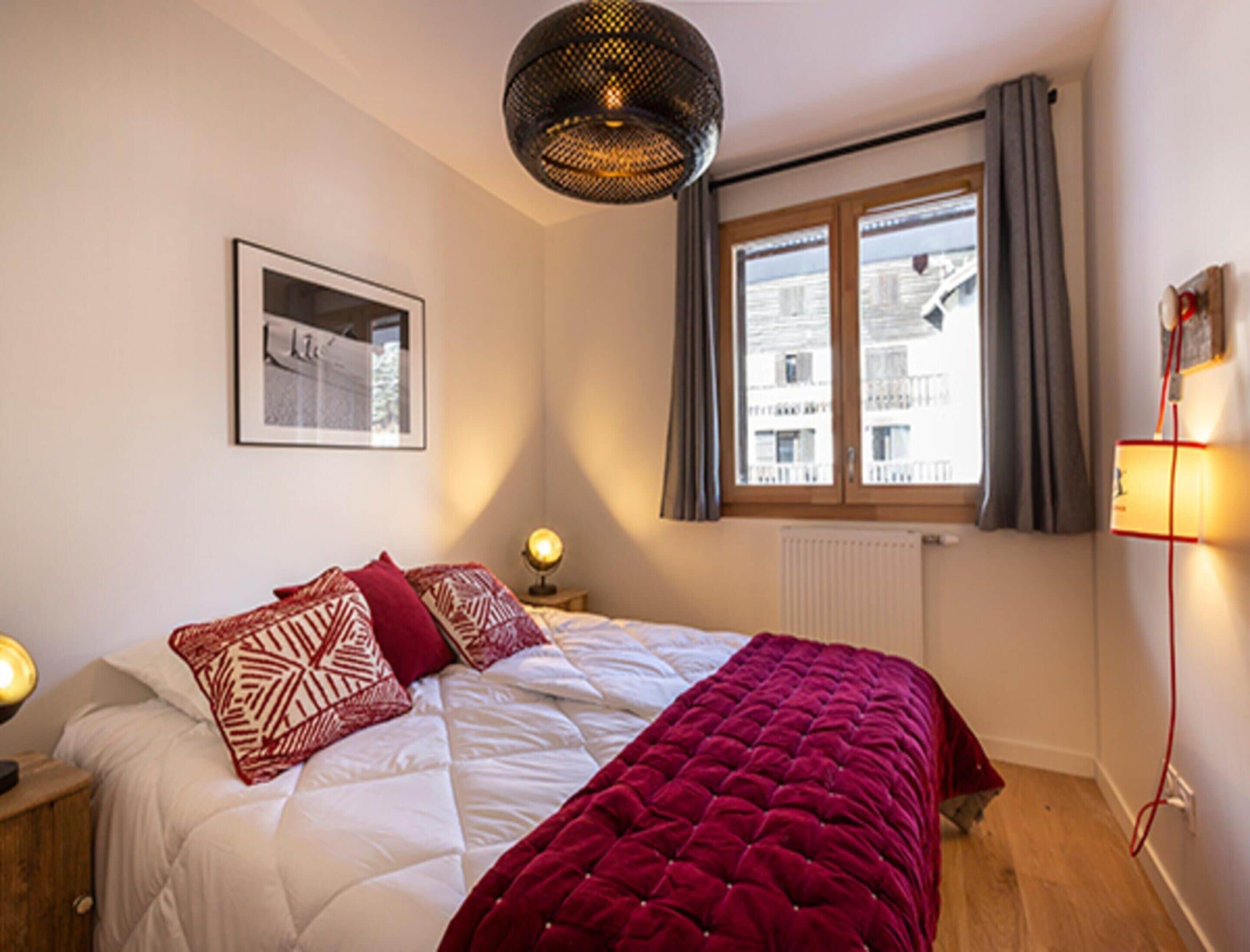 Un dormitorio con una cama, una ventana con cortinas, una lámpara de pared e imagen enmarco.