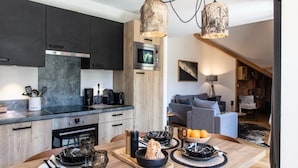 A modern kitchen with dark cabinets, a wooden dining table set with plates, glasses, and a bowl of fruit. - Chalet in Vaujany With Panoramic Mountain Views (Vaujany)