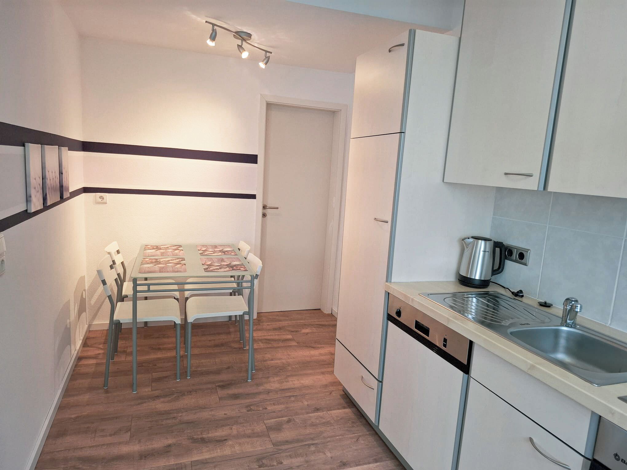 A compact kitchen with a dining table, chairs, a sink, and a kettle.
