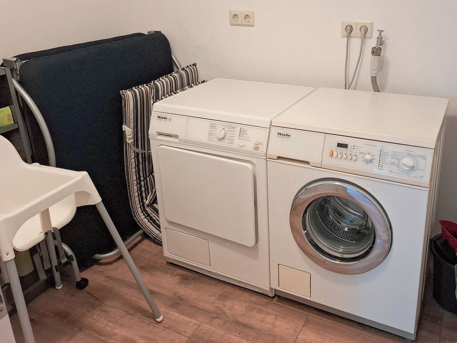 Un espacio de lavandería compacto con una lavadora Miele de carga frontal, una silla plegable y un tendedero.