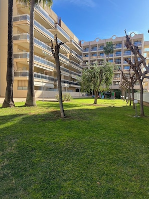 A multi-story building with balconies, a grassy courtyard, and a sculpture.