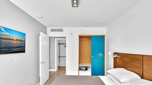 Una habitación de hotel moderna con cama, mesita de noche y vista al mar desde una puerta abierta.