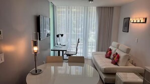 Una sala de estar moderna con un sofá blanco, una mesa redonda y un televisor montado en la pared.