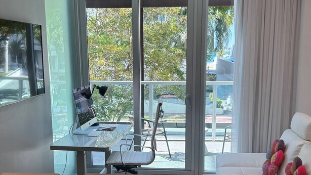 Una sala de estar moderna con un sofá blanco, una mesa de comedor con sillas y un balcón con vistas al exterior.