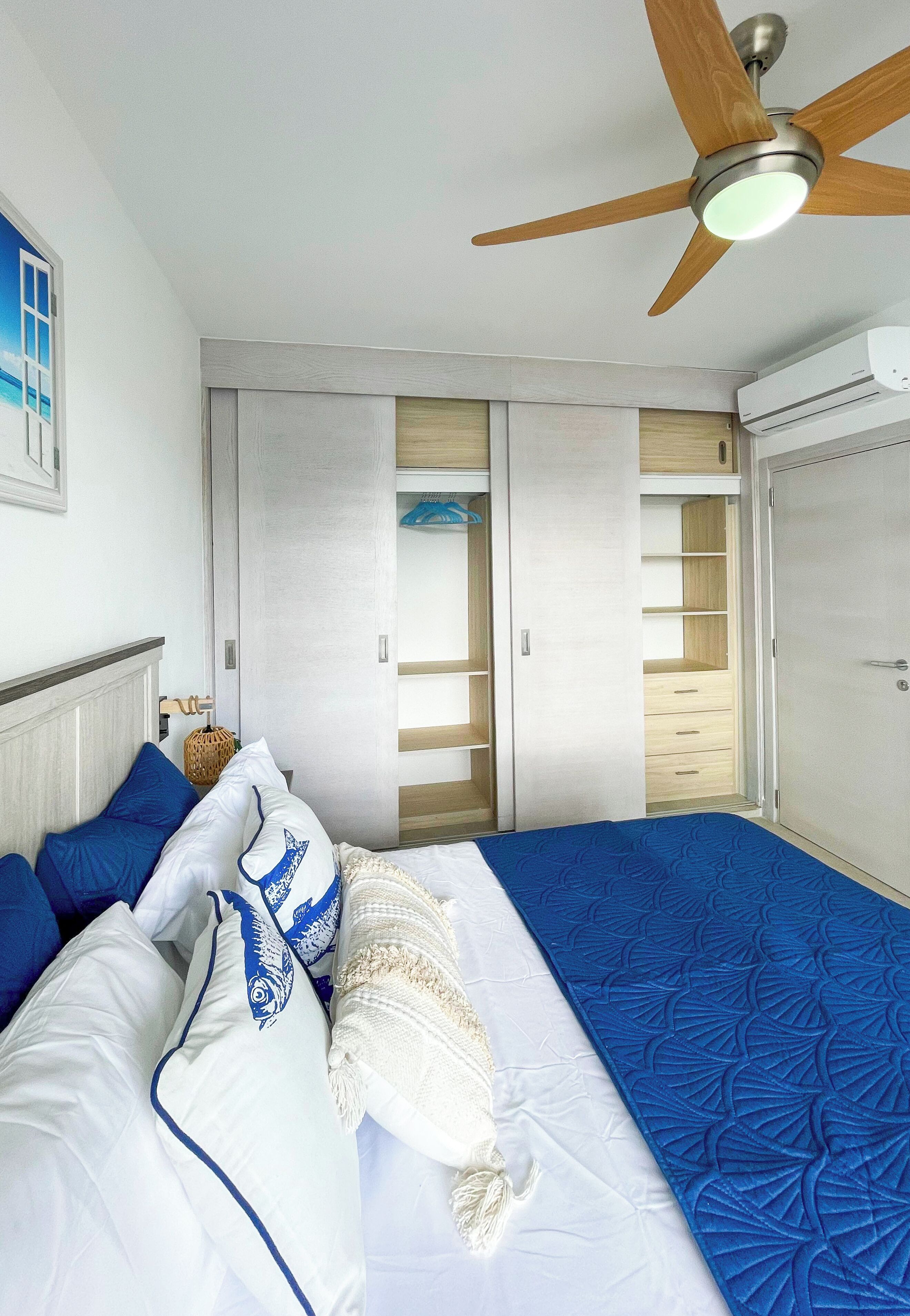 A bedroom with a bed, a ceiling fan, and a wardrobe with open doors.
